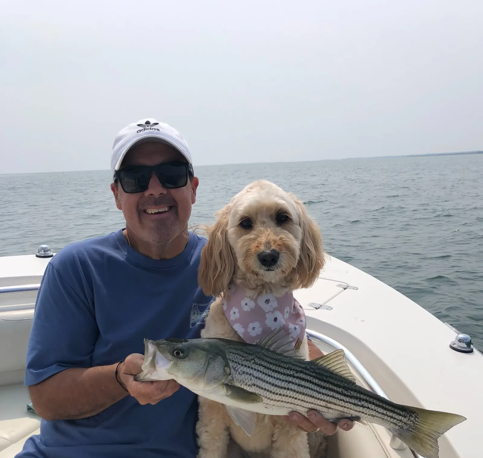 Captain Renato and Carli holding a striped bass aboard Last Captain